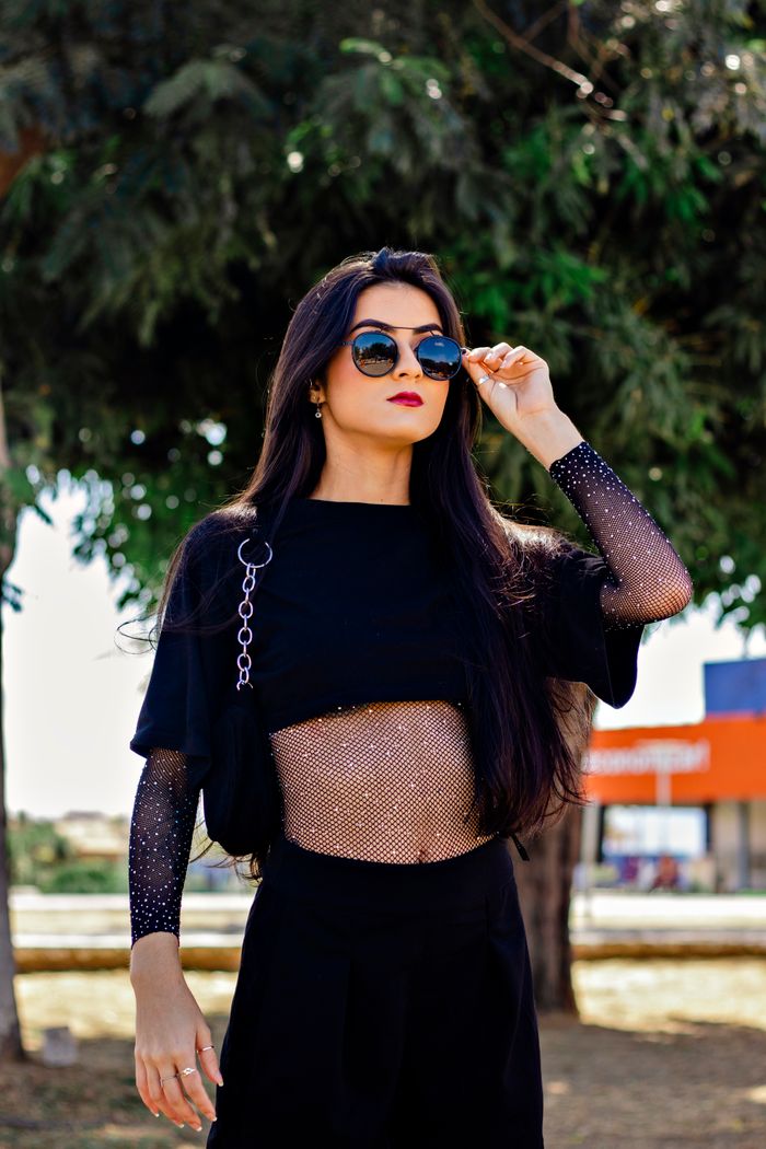 Confident woman with long hair in elegant black outfit and sunglasses standing outside.