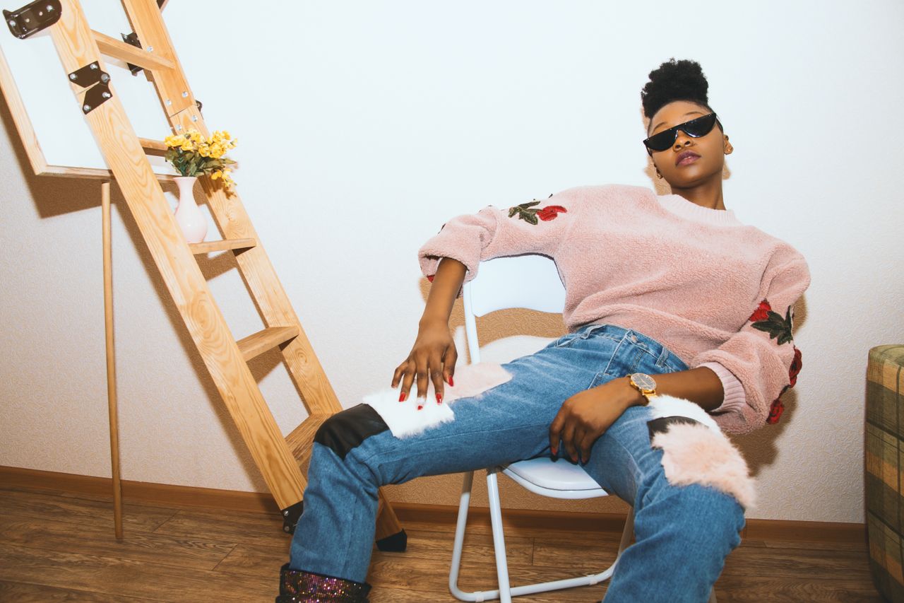 Trendy woman poses stylishly in a chic outfit with blue jeans and a decorative sweater indoors.